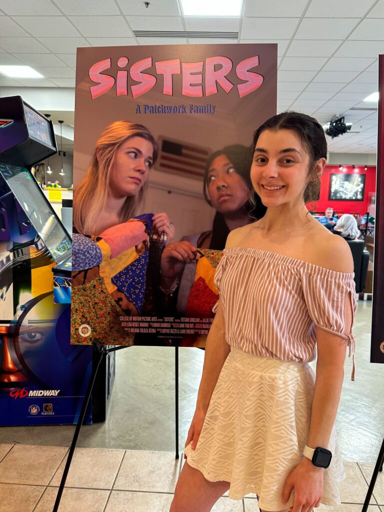 Girl in a white skirt and pink shirt standing in front of a movie poster.