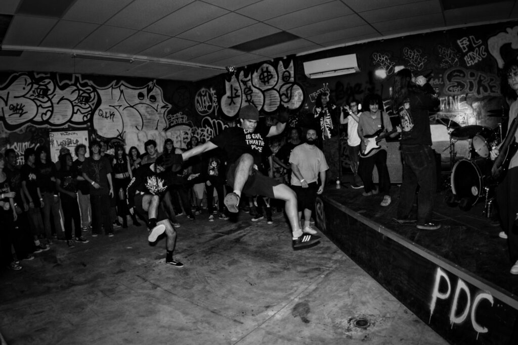 black and white photo of teenager jumping off stage into a mosh pit