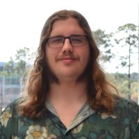 Man with long hair in a Hawaiian shirt stands outside