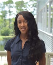 Image of woman with long-hair, blue short-sleeve top, with outside background.