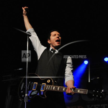 Adam Young holding a black guitar with his hand in the air on stage.