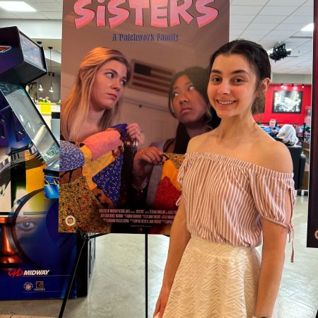 Girl in a white skirt and pink shirt standing in front of a movie poster.